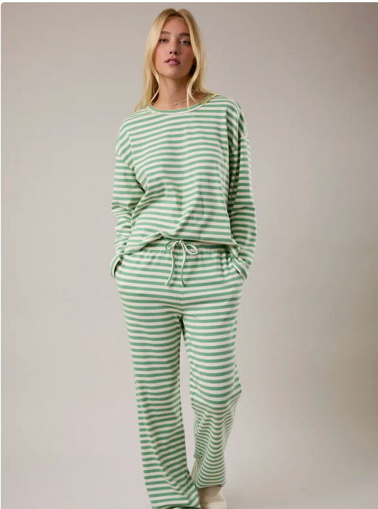 Woman wearing a long sleeve green and white striped pajama set against a plain background.
